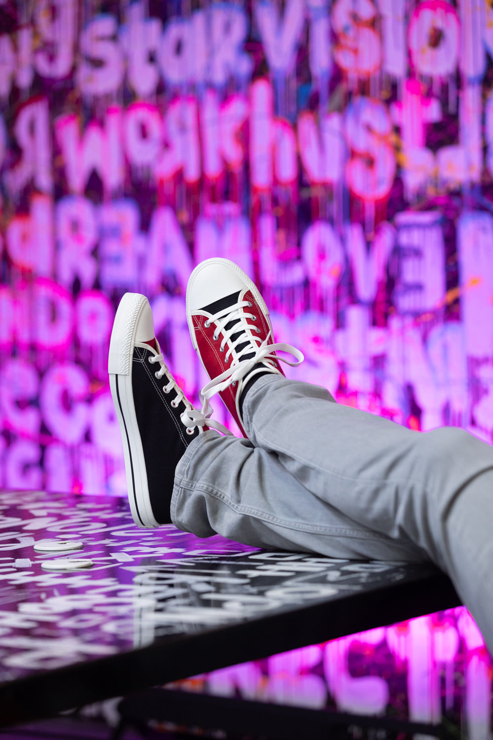 Red and black mismatched sneakers worn by person with feet up on table against colorful graffiti background