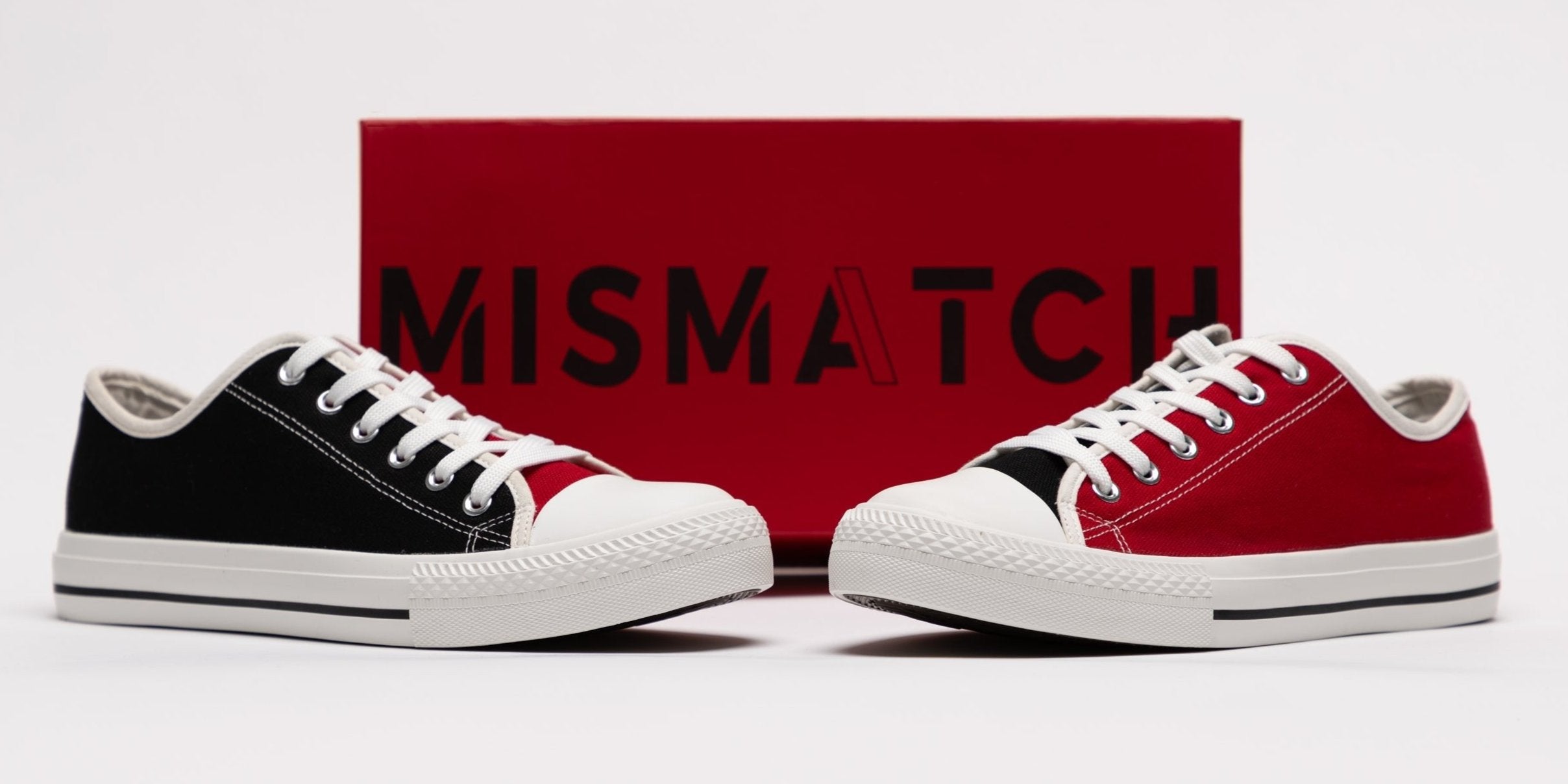 Red and black mismatched sneakers displayed in front of a red Mismatch Shop shoe box with a white background